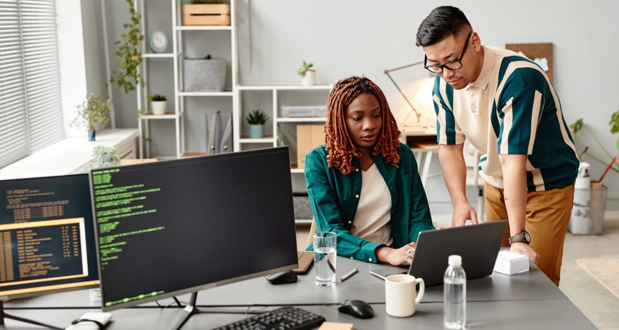 Portrait of two IT developers reviewing code on computer screen in office, female QA engineer at work